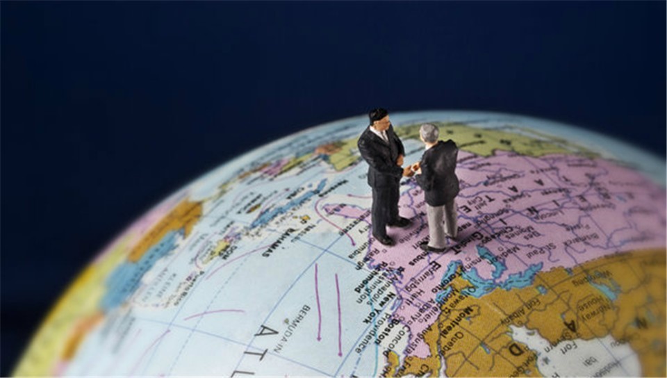 Two miniature politicians shake hands standing on a globe