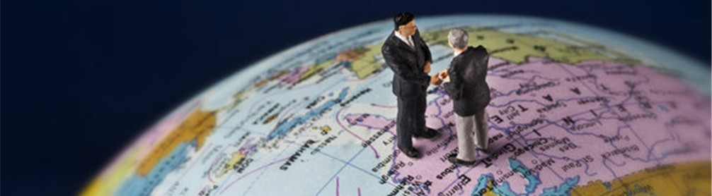 Two miniature politicians shake hands standing on a globe